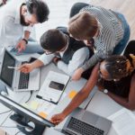 A group of people huddled around a laptop in an office setting.